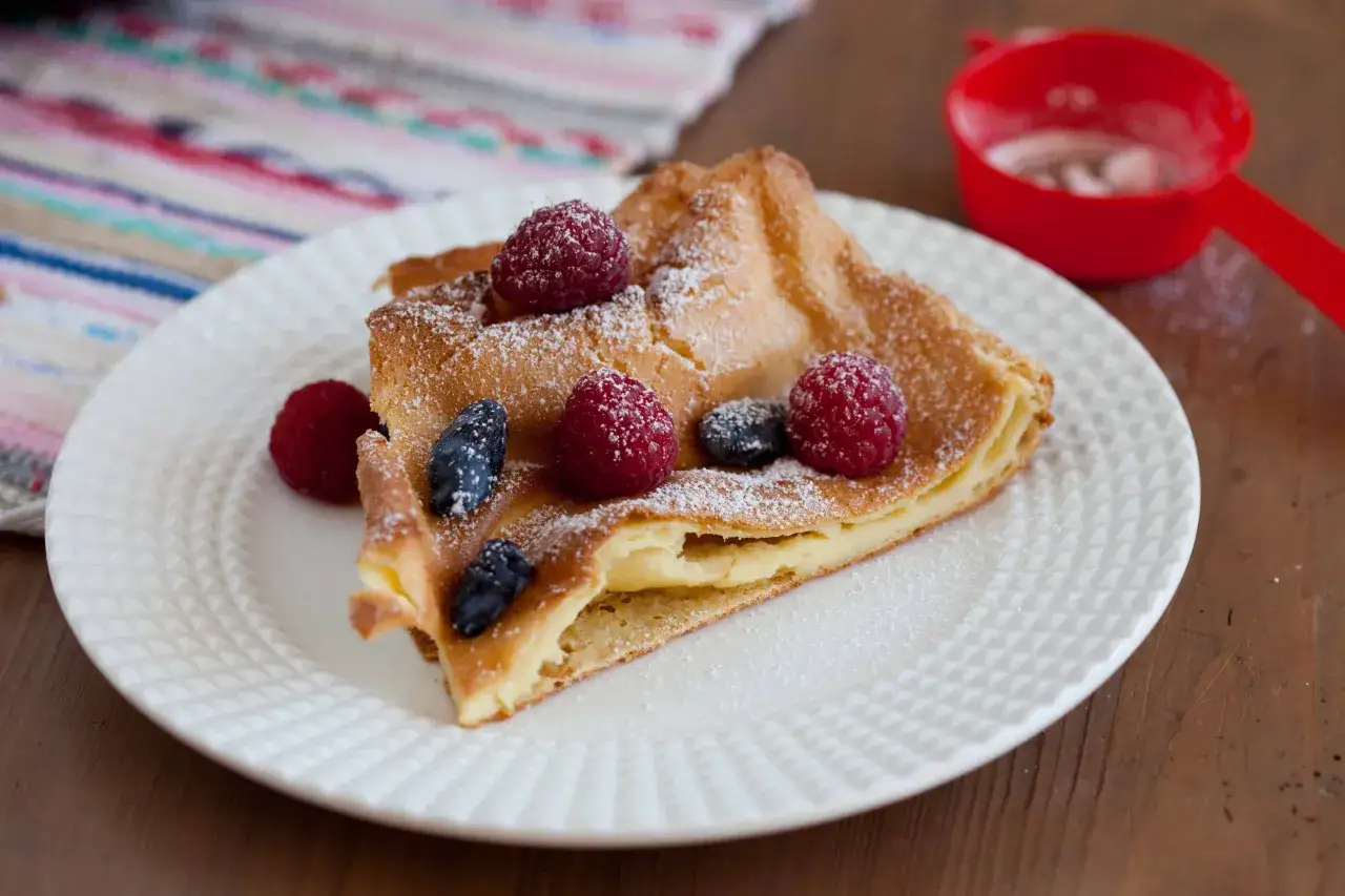 Pyszny, puszysty dutch baby z malinami i borówkami, posypany cukrem pudrem. Idealny na śniadanie.