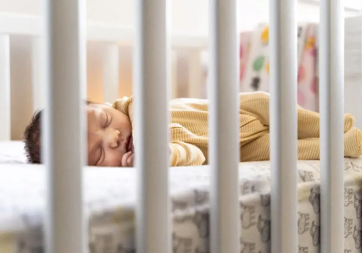 En 1 m&aring;nads bebis sover inte, utan ligger vaken i sin spj&auml;ls&auml;ng, kl&auml;dd i en gulrandig pyjamas.