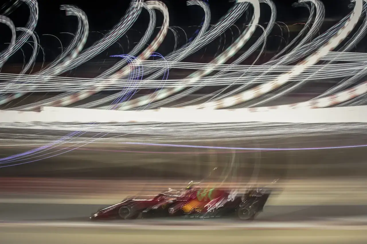 Rozmyty czerwony bolid F1 pędzi nocą, zostawiając za sobą smugi świateł. To kwintesencja tego, co to F1 – prędkość i widowisko.
