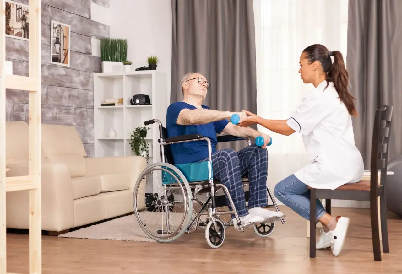 Terapeuta ayuda a un hombre en silla de ruedas a hacer ejercicio con pesas, apoyándolo en su recuperación de **la enfermedad**.