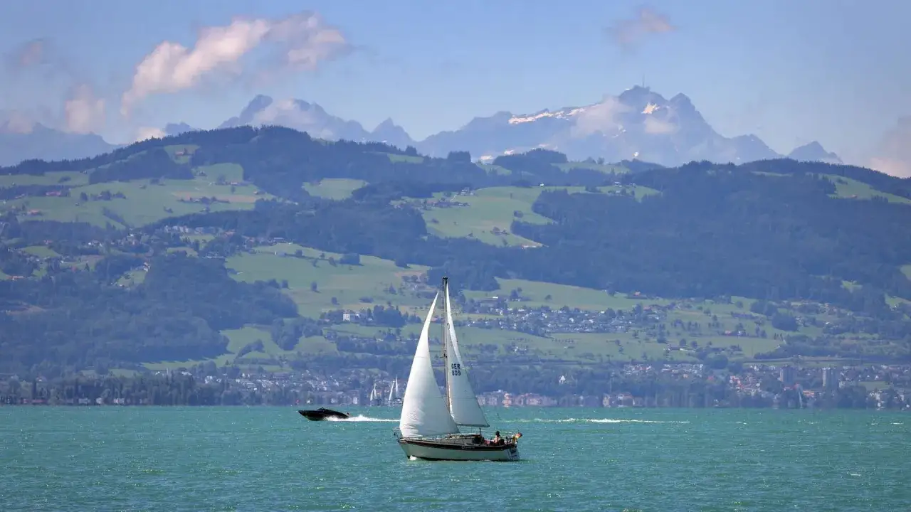 Segelboot auf türkisfarbenem Wasser vor malerischer Alpenkulisse mit grünen Hügeln und schneebedeckten Gipfeln – ein Bild wie aus einem Traum Reiseziele.