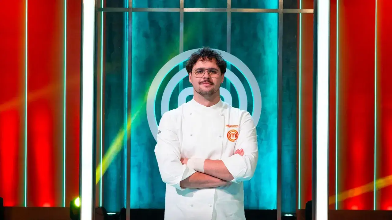 Matteo, vincitore MasterChef 15, posa con la divisa da chef, braccia conserte, davanti al logo del programma.