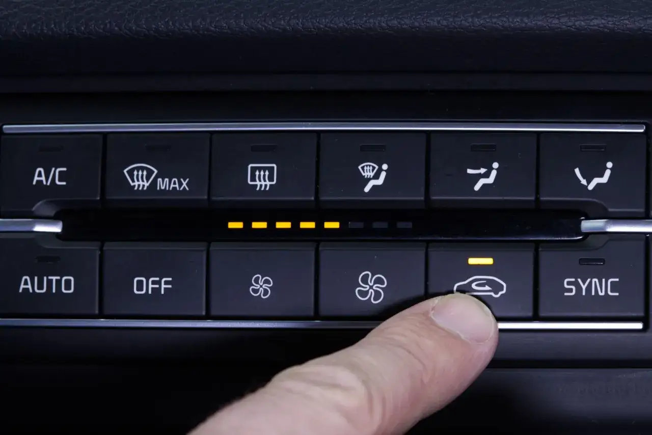 Finger drückt auf Klimaanlagen-Symbol im Cockpit Auto. Gelbe Lichter zeigen die Einstellungen an.