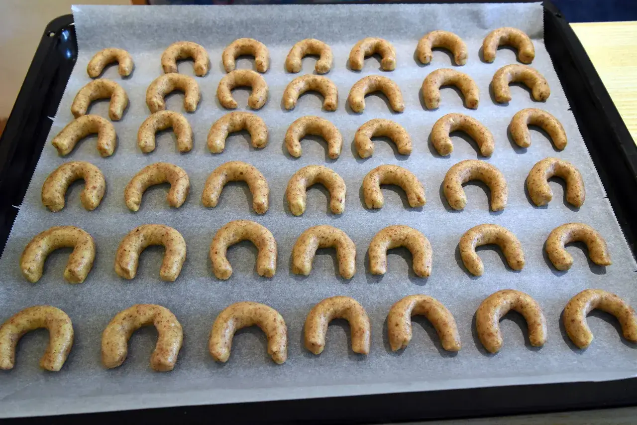 Reihe um Reihe liegen goldbraune Vanillekipferl auf Backpapier.