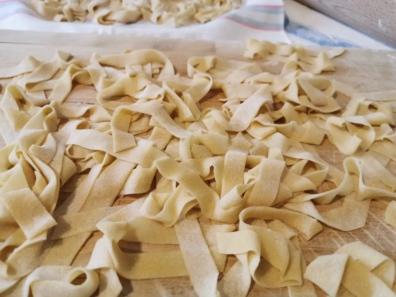 Tagliatelle fatte in casa, fresche e pronte per essere cucinate, sparse su un tagliere di legno.