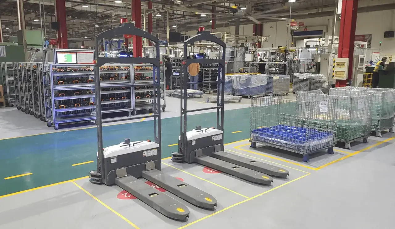Dwa autonomiczne wózki widłowe agv robot stoją na hali produkcyjnej, gotowe do transportu towarów.