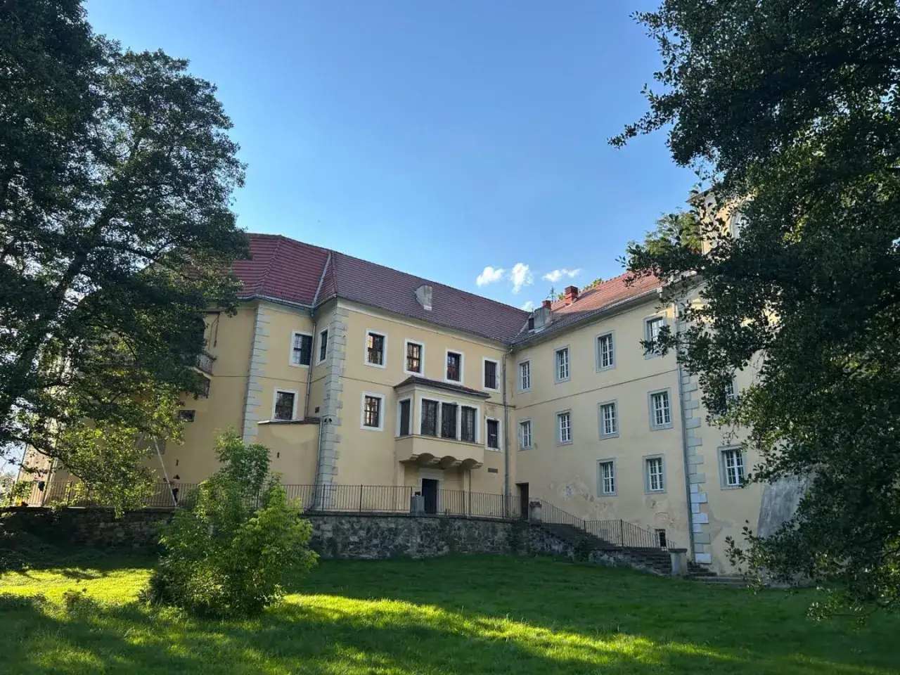 Ż&oacute;łty zamek na skale w Trzebieszowicach, otoczony zielenią, z czerwonym dachem i licznymi oknami, prezentuje się okazale.
