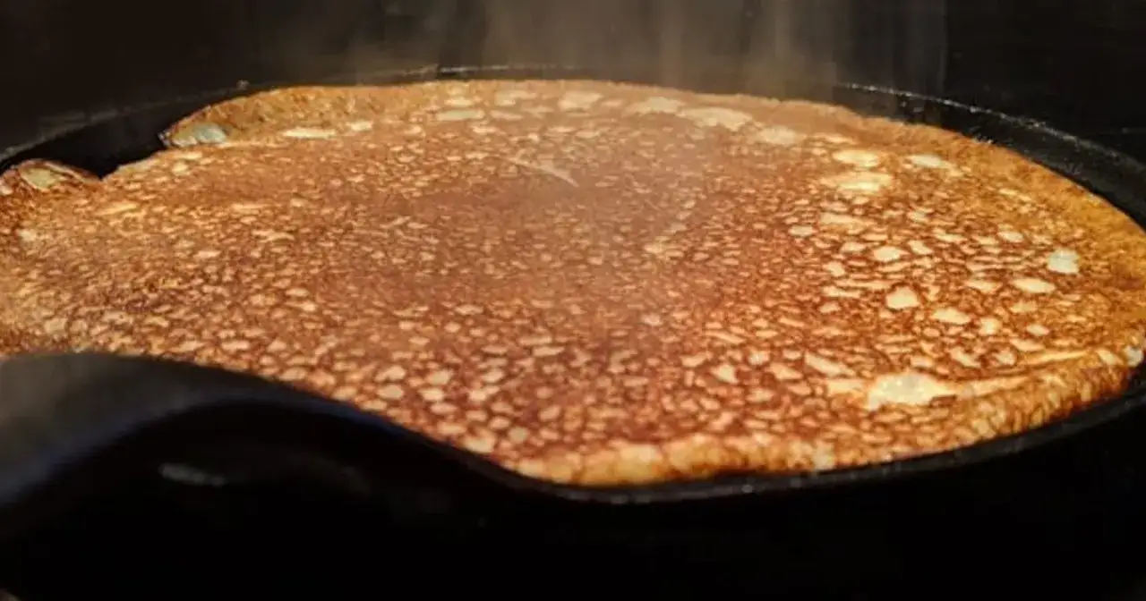 En gyllene, nygräddad pannkaka steker i en gjutjärnspanna. Perfekt för en mysig frukost med glutenfria pannkakor.
