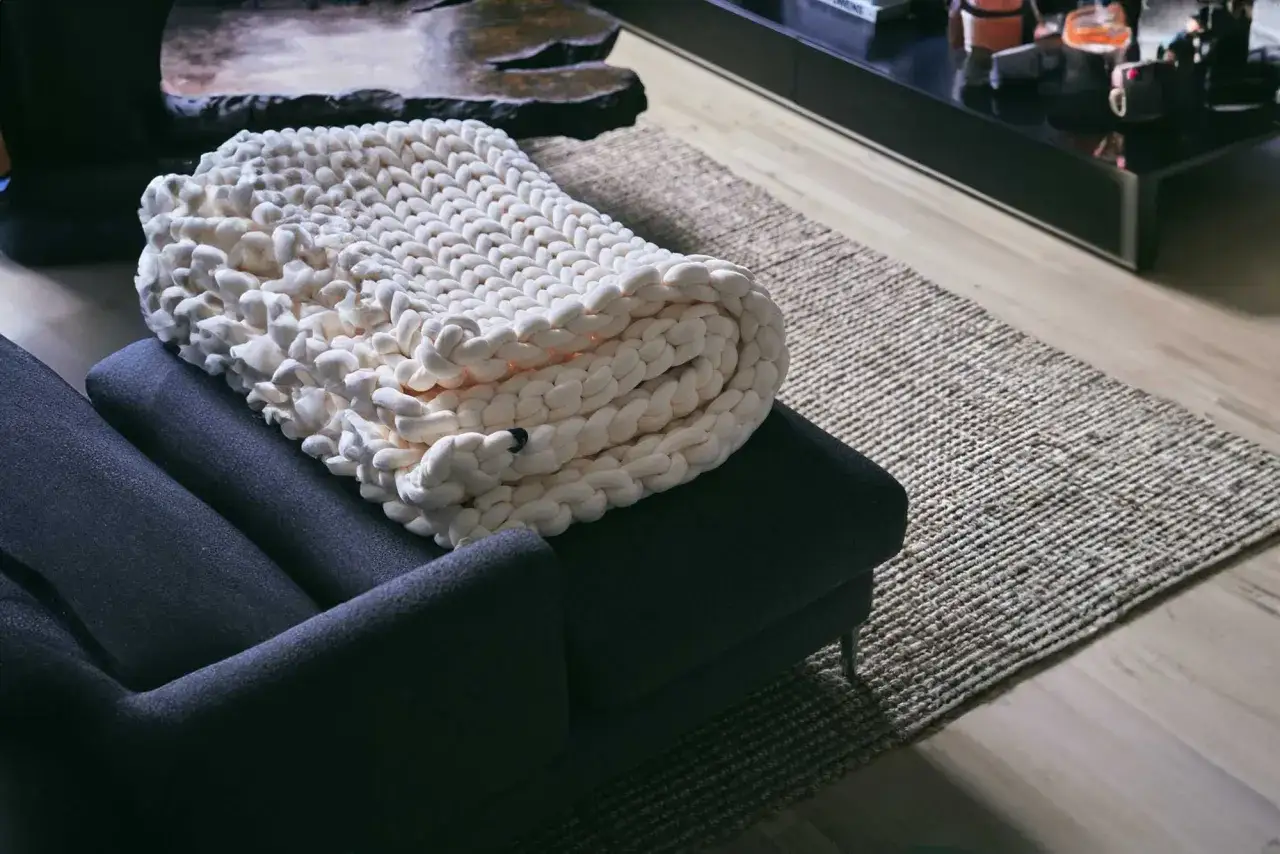 A chunky knit weighted blanket is draped over a dark grey armchair. Learn how to dry a weighted blanket to keep it fresh and cozy.