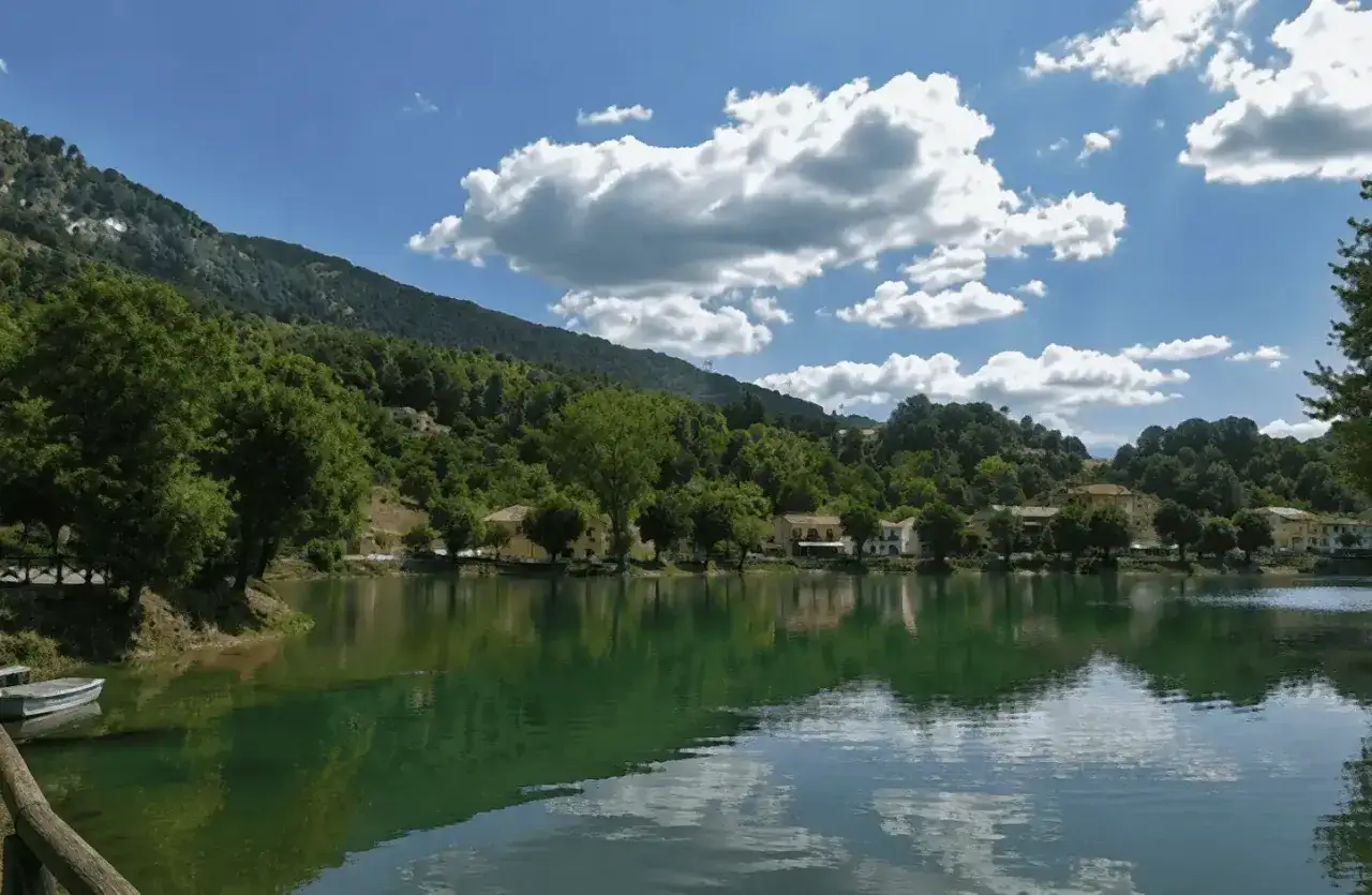 Il **lago Sirino** riflette il cielo azzurro e le case colorate, circondato da colline verdi e alberi lussureggianti.