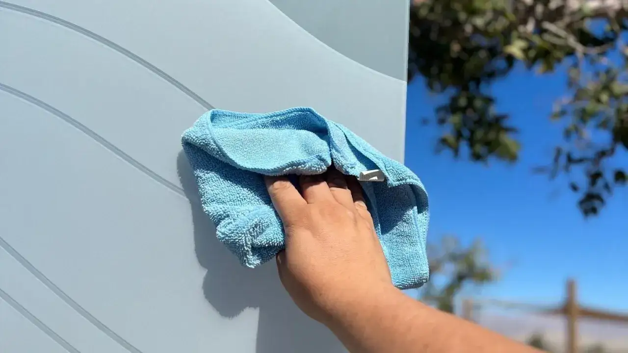 Mano limpiando una puerta lacada en blanco con un pa&ntilde;o azul. Aprende c&oacute;mo limpiar puertas lacadas en blanco f&aacute;cilmente.