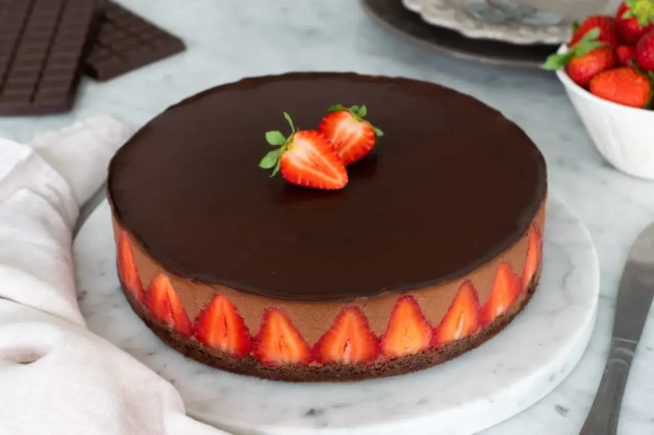 Torta con fragole e cioccolato, un capolavoro goloso con fragole fresche disposte lungo il bordo e due mezze fragole sulla lucida copertura al cioccolato.