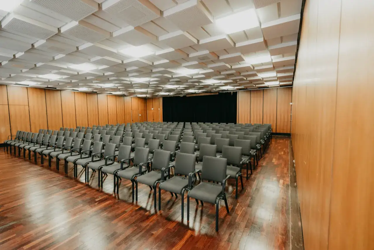 Leere Reihen grauer St&uuml;hle im **Theater und Konzerthaus Solingen**. Der Holzboden gl&auml;nzt, die Decke ist mit Schallschutzpaneelen verkleidet.