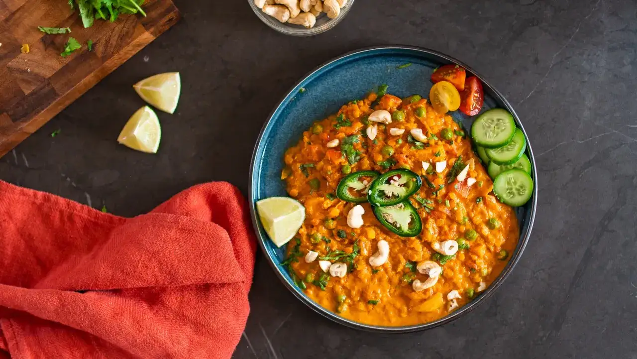 Herzhaftes rote Linsen Curry mit Erbsen, Cashewkernen, Jalapeños, Limette und Gurkenscheiben.