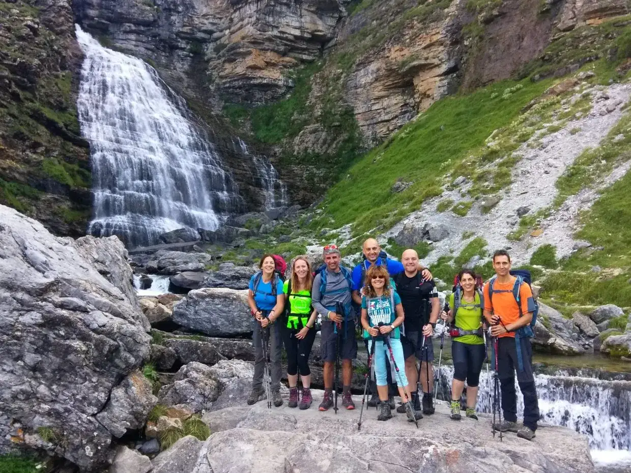 Grupo de excursionistas posando frente a una cascada en los montes Pirineos.