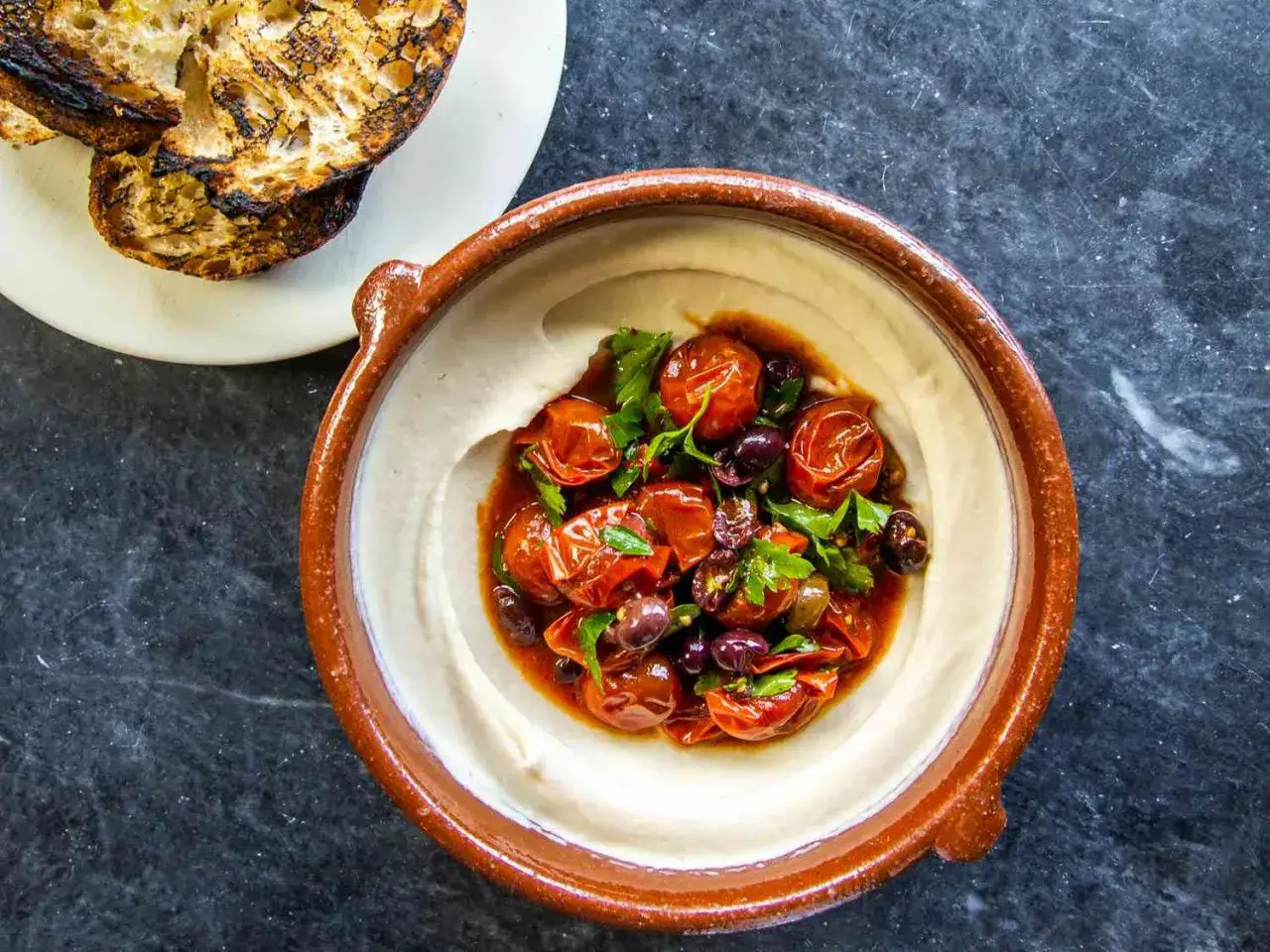 Cremiger veganer tomatenaufstrich mit Oliven und Petersilie, serviert mit geröstetem Brot.