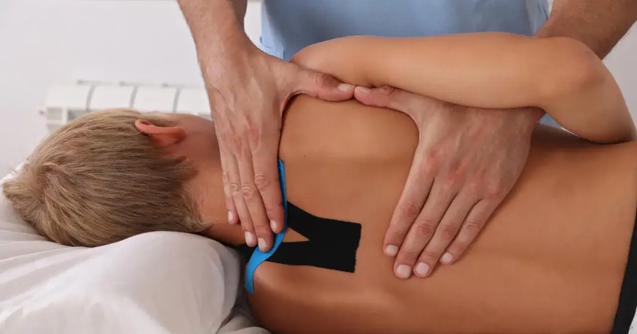 Fizjoterapeuta aplikuje taśmy kinezjotaping na plecy pacjenta z chorobą Scheuermanna, wspierając leczenie.
