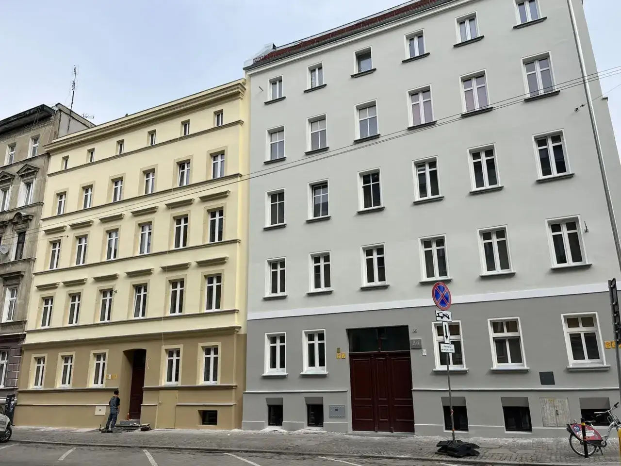 Eleganckie kamienice, jedna żółta, druga szara, czekają na dotację na remont mieszkania.