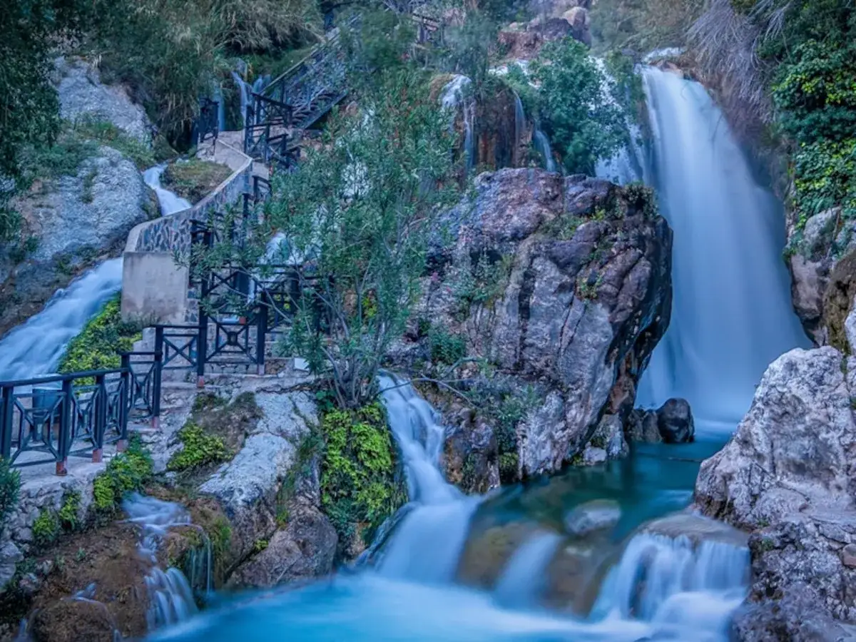 Cascada y escaleras de madera en las fuentes del Algar, con agua cayendo en cascada y vegetación exuberante.