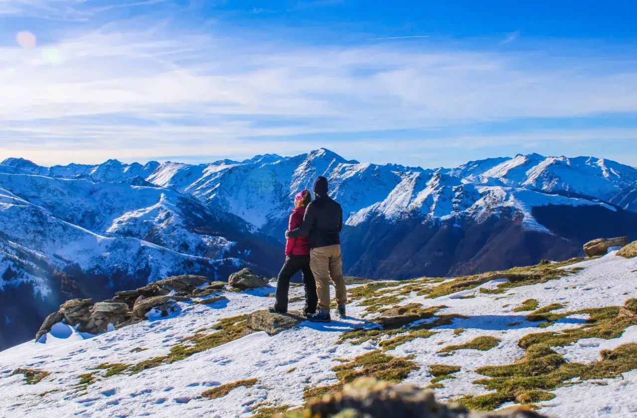 Couple admirant le panorama enneigé depuis le pic de Gleize. Les montagnes bleues s'étendent à perte de vue sous un ciel clair.