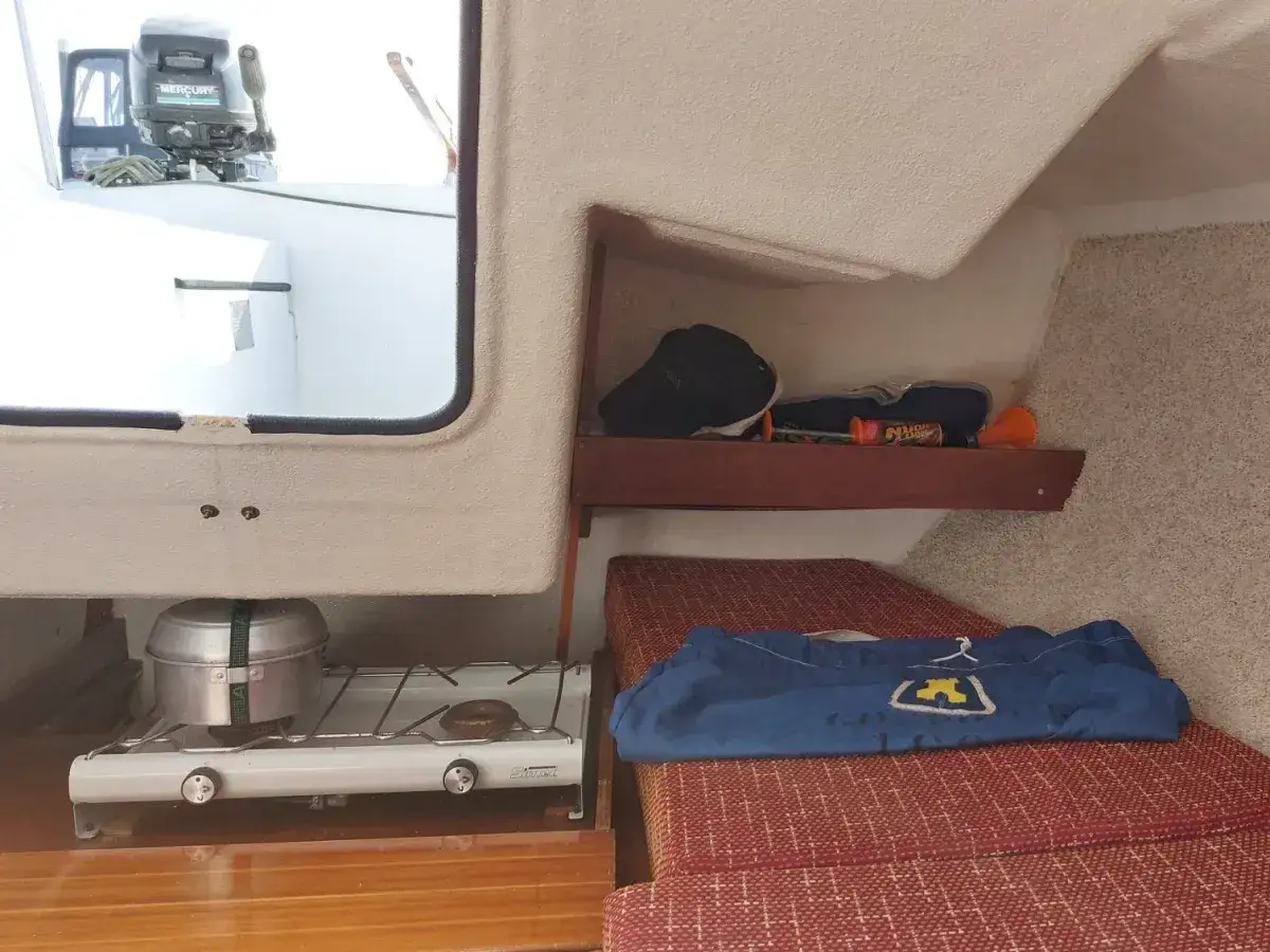 Intérieur du Kelt 550 : réchaud, lit avec couverture bleue, étagère avec chaussures et objets divers.