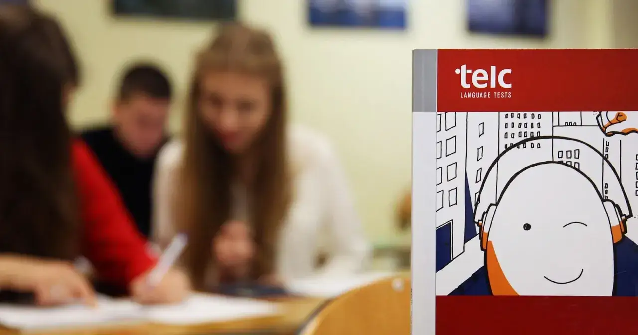 Studenci piszą egzamin. Czy wiesz, ile trwa sesja na studiach? Obok podręcznik do języków obcych.
