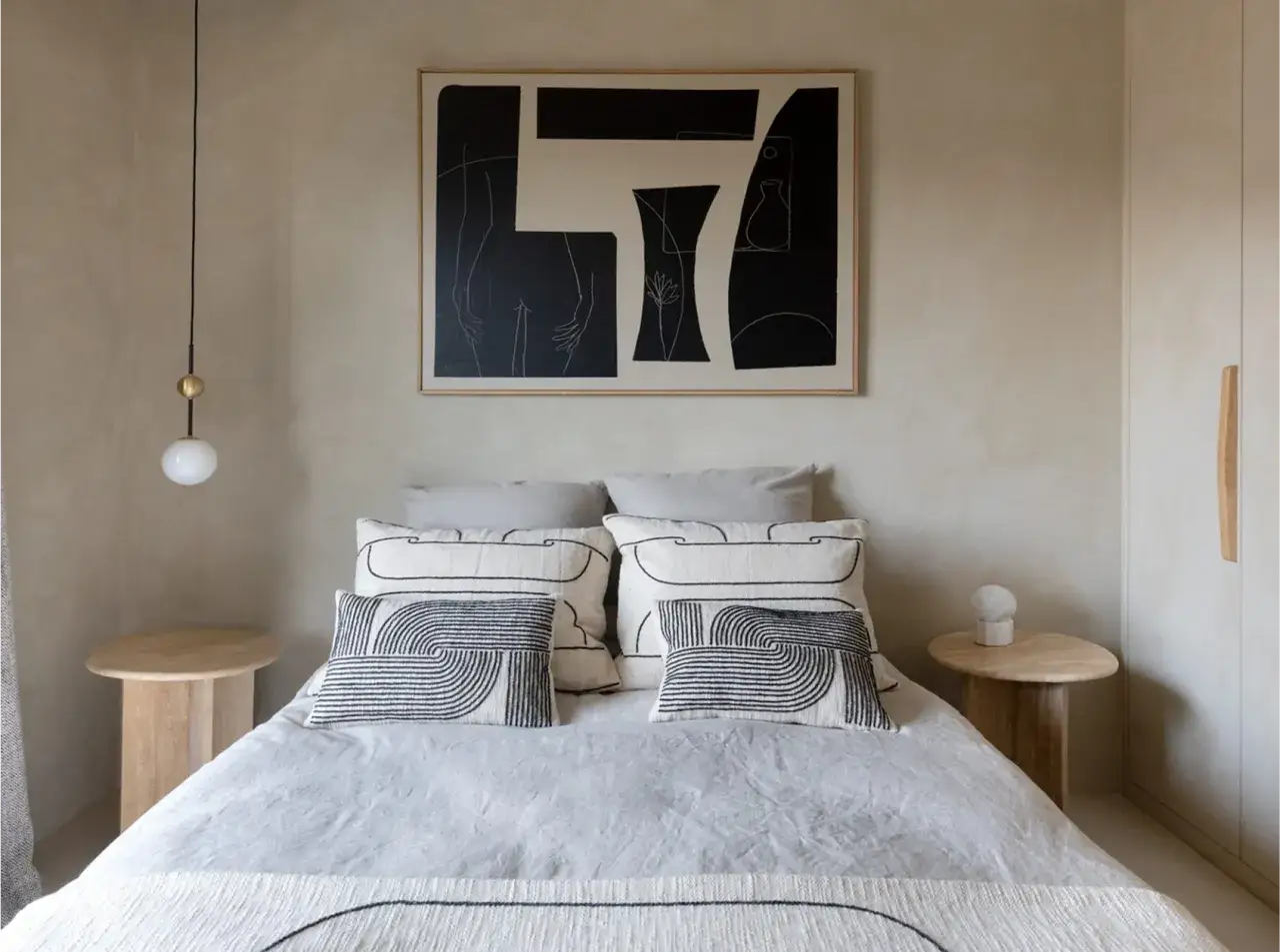 Dormitorio con cama vestida, cuadros abstractos y l&aacute;mpara colgante. Las paredes tienen un acabado de pintura a la cal.