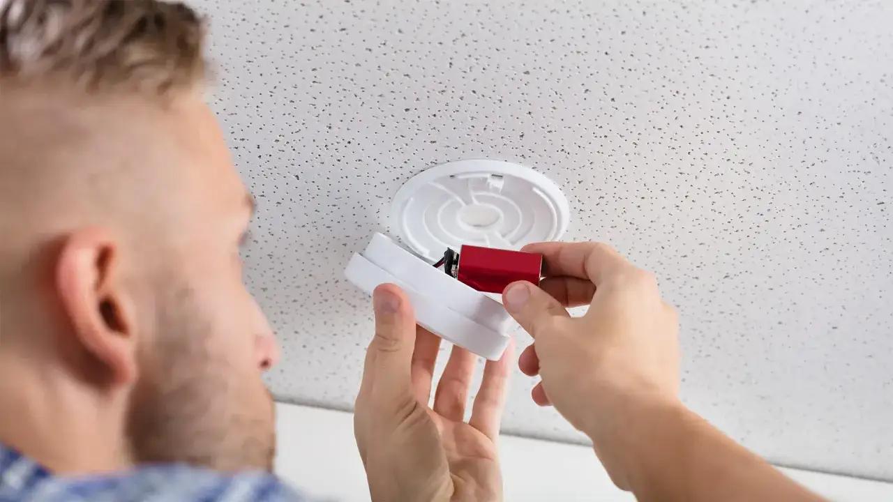 Mann wechselt Batterie im Rauchmelder. Ein funktionierender Rauchmelder ist wichtig, um fr&uuml;hzeitig vor Brandrauch gewarnt zu werden und Anzeichen von Rauchvergiftung zu vermeiden.