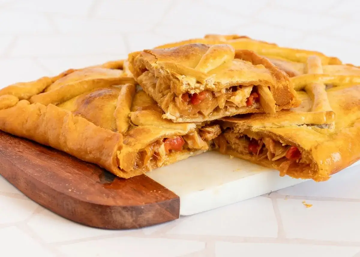 Empanada gallega dorada y crujiente, cortada para mostrar su relleno de atún y pimientos.