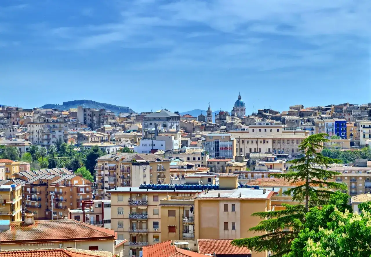 Panoramica di **Caltanissetta cosa vedere**: tetti rossi, palazzi colorati e la cupola di una chiesa sotto un cielo azzurro.