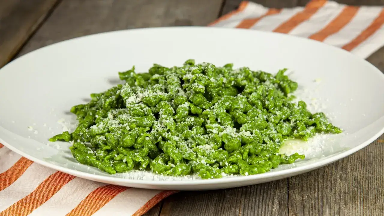 Un piatto di gnocchi di spinaci freschi, conditi con parmigiano grattugiato, su un tovagliolo a righe arancioni e bianche.