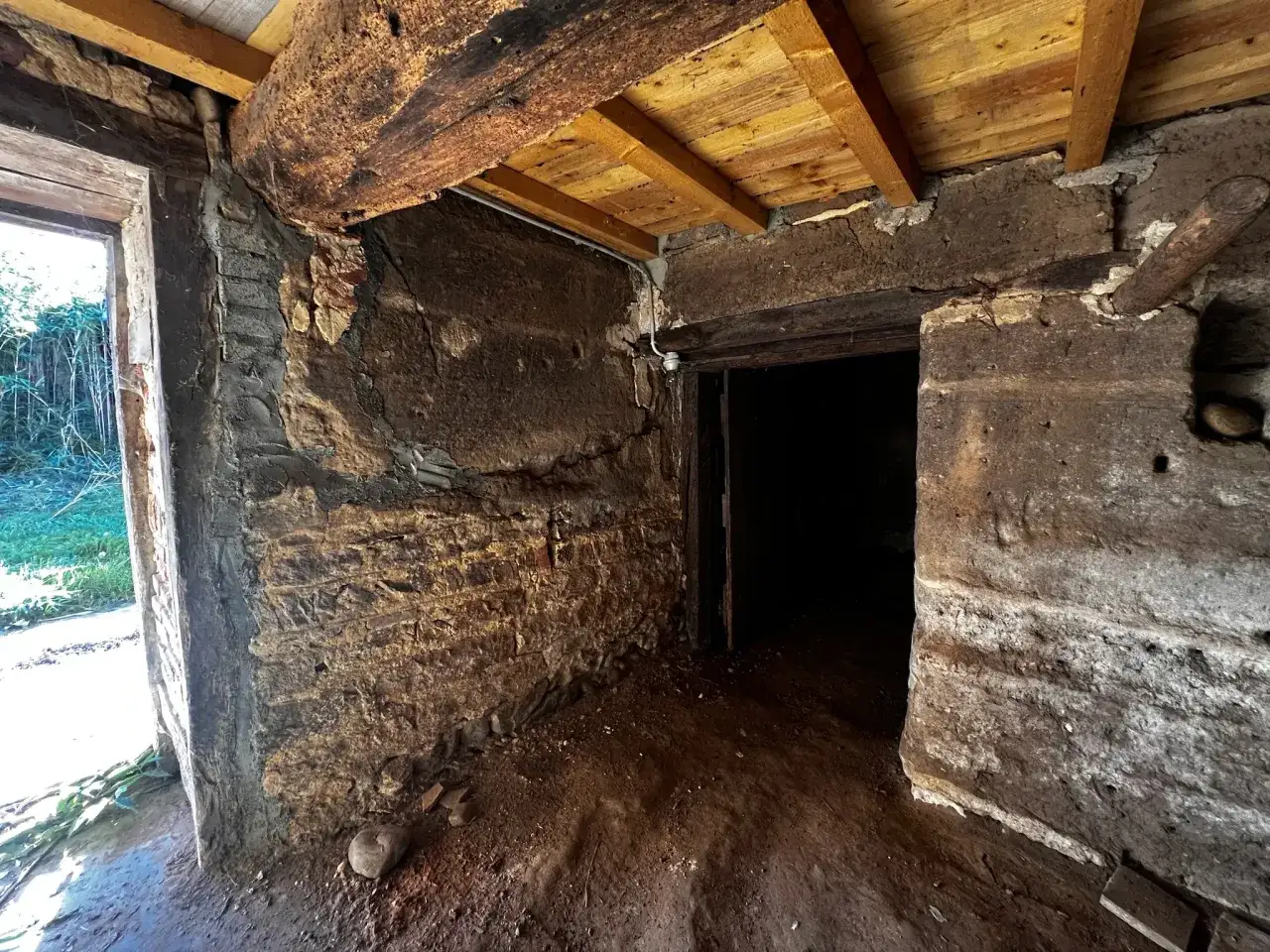 Intérieur d'une maison en pisé en ruine, poutres apparentes, murs dégradés. Danger de chute.