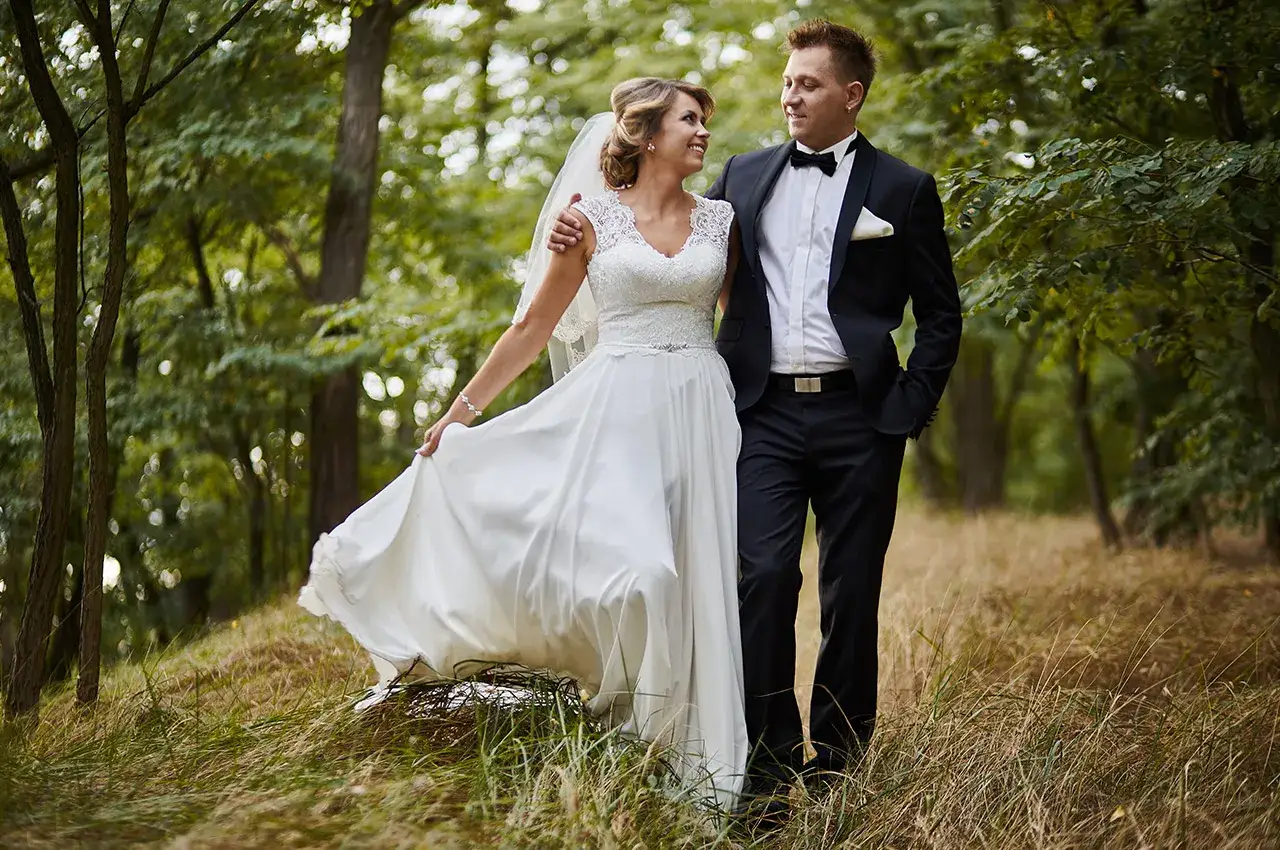 Para młoda spaceruje po lesie, ciesząc się chwilą przed ślubem. Panna młoda w pięknej sukni, pan młody w eleganckim garniturze.