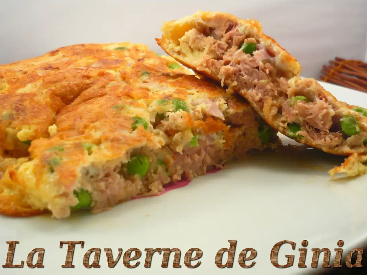 Une omelette au thon généreuse, garnie de petits pois, coupée en deux pour révéler sa texture moelleuse. Un délice simple et savoureux.
