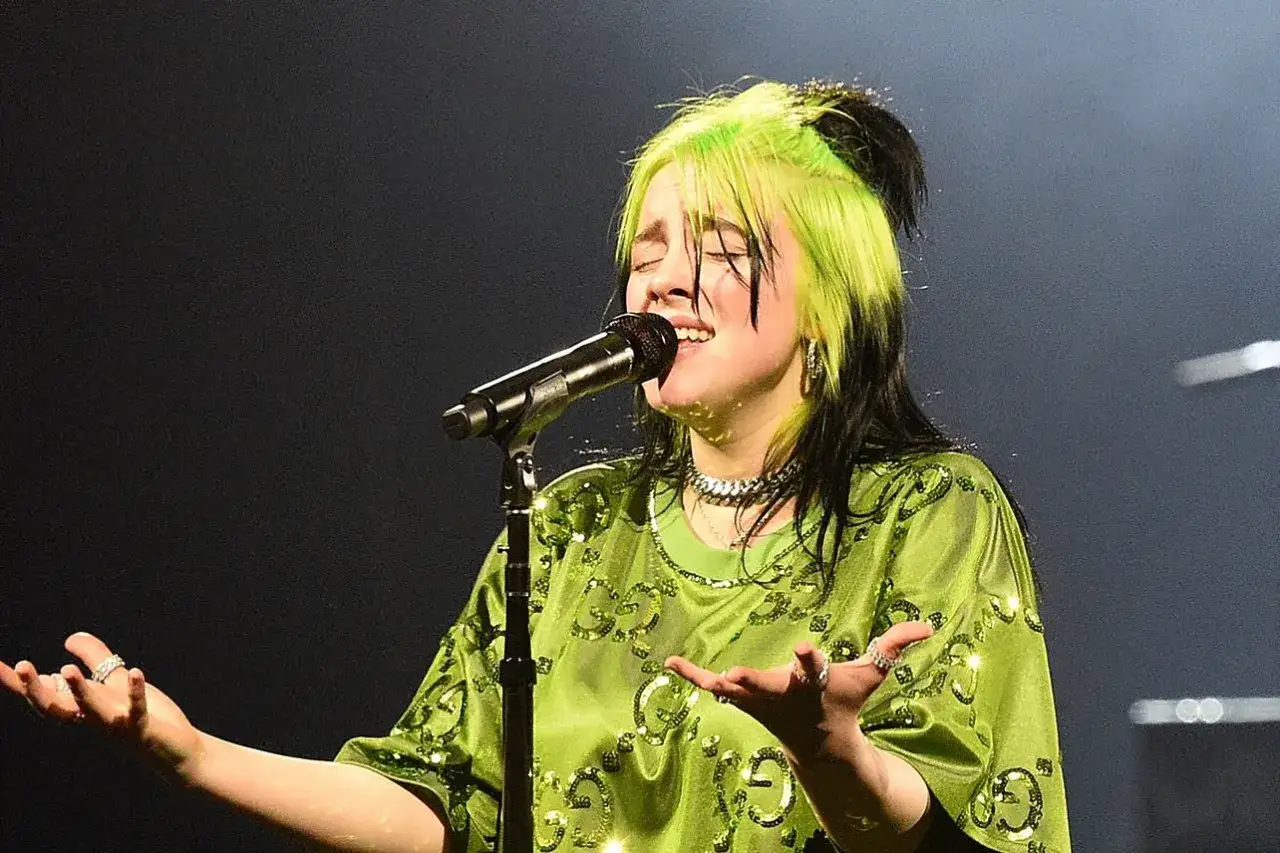 Billie Eilish, con i suoi capelli verdi e neri, canta sul palco. Il suo genere musicale &egrave; unico, un mix di pop alternativo e dark pop.