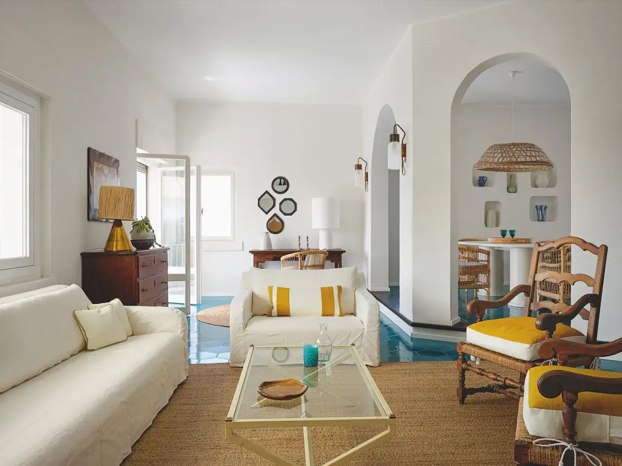 Soggiorno luminoso con divani bianchi, tappeto in juta e dettagli in vimini, che evocano un autentico stile mediterraneo contemporaneo.