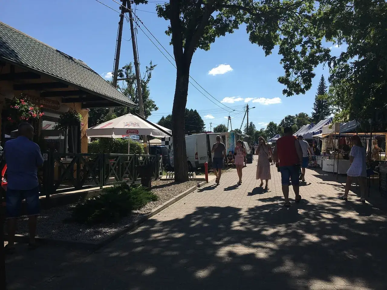 Tleń atrakcje dla dzieci: jarmark z kramami, restauracja i spacerujący ludzie w słoneczny dzień.