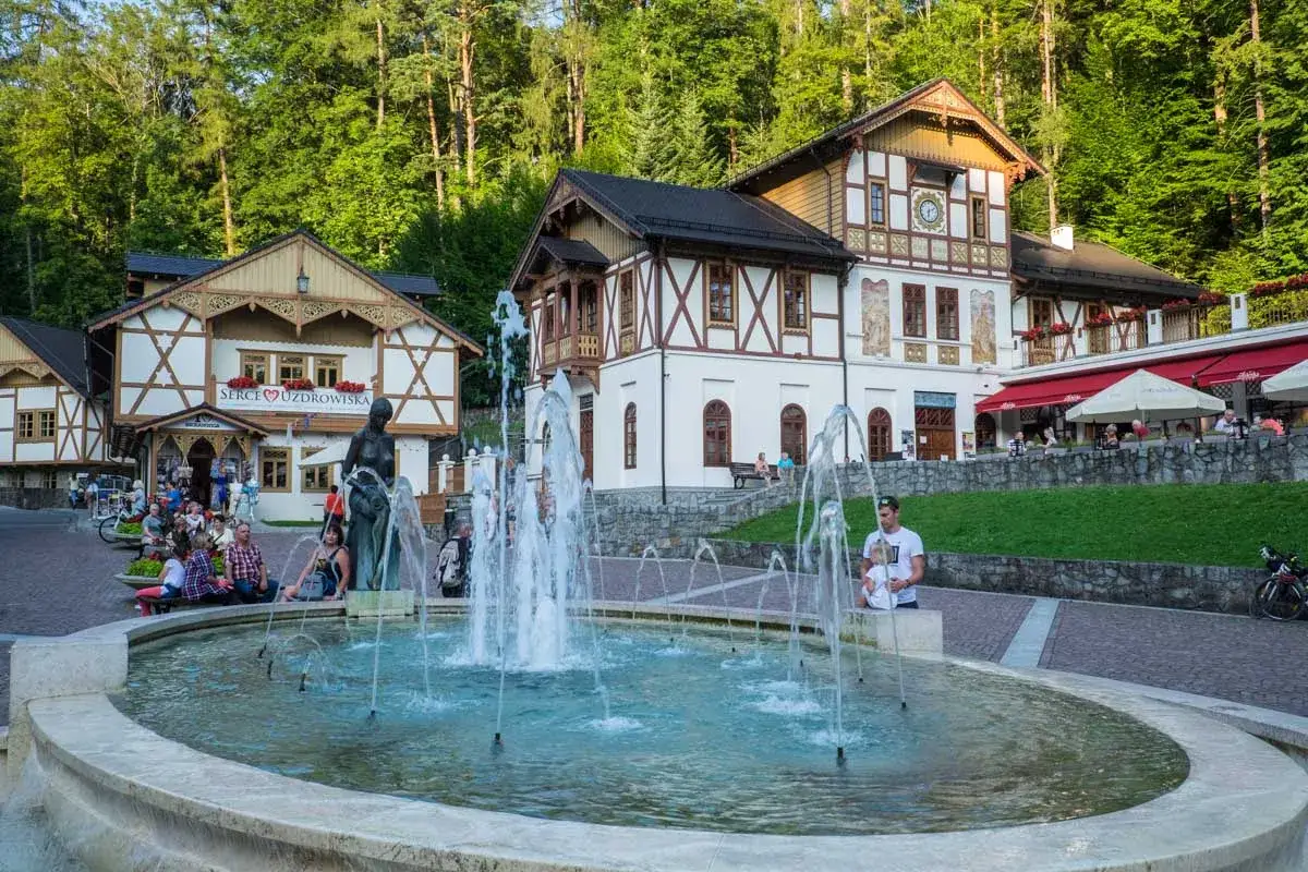 Szczawnica atrakcje: fontanna i urokliwe budynki w stylu góralskim, otoczone zielenią.