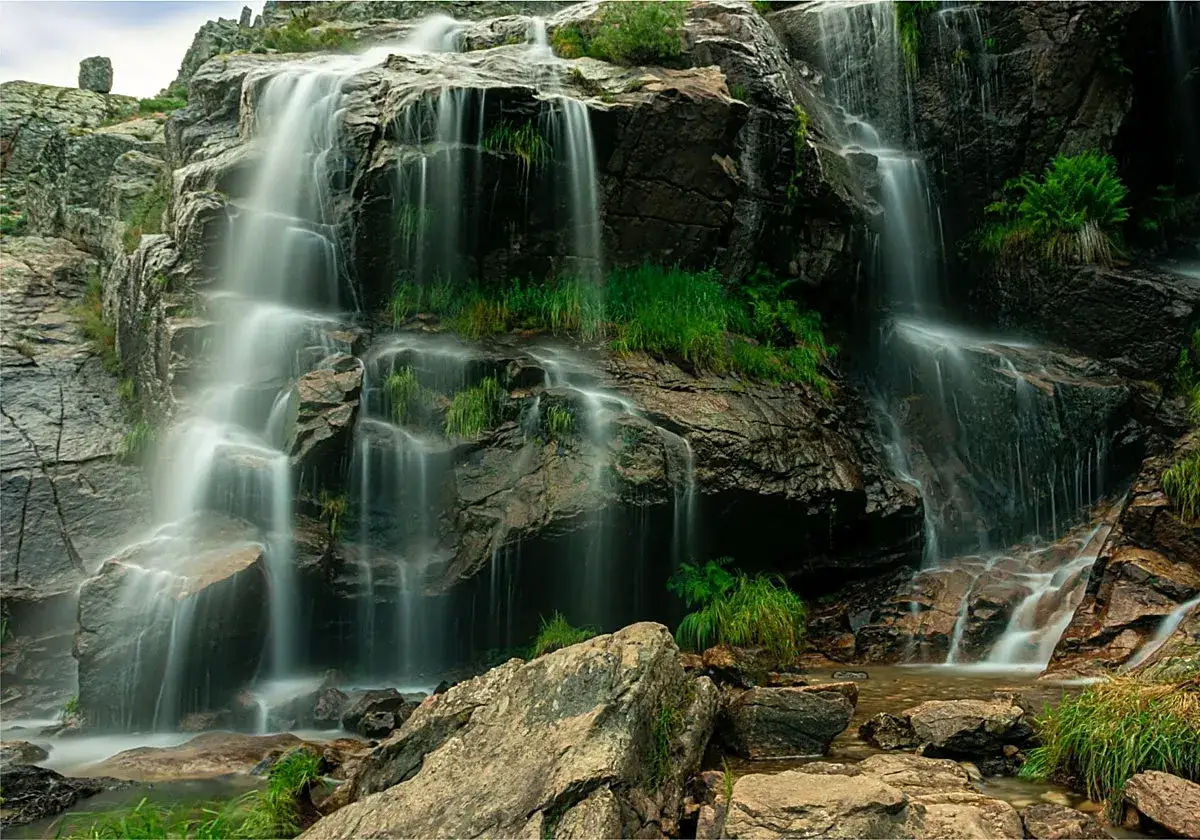 Cascadas espectaculares, un oasis natural cerca de Madrid. El agua desciende por rocas cubiertas de musgo y vegetación, creando un paisaje sereno.