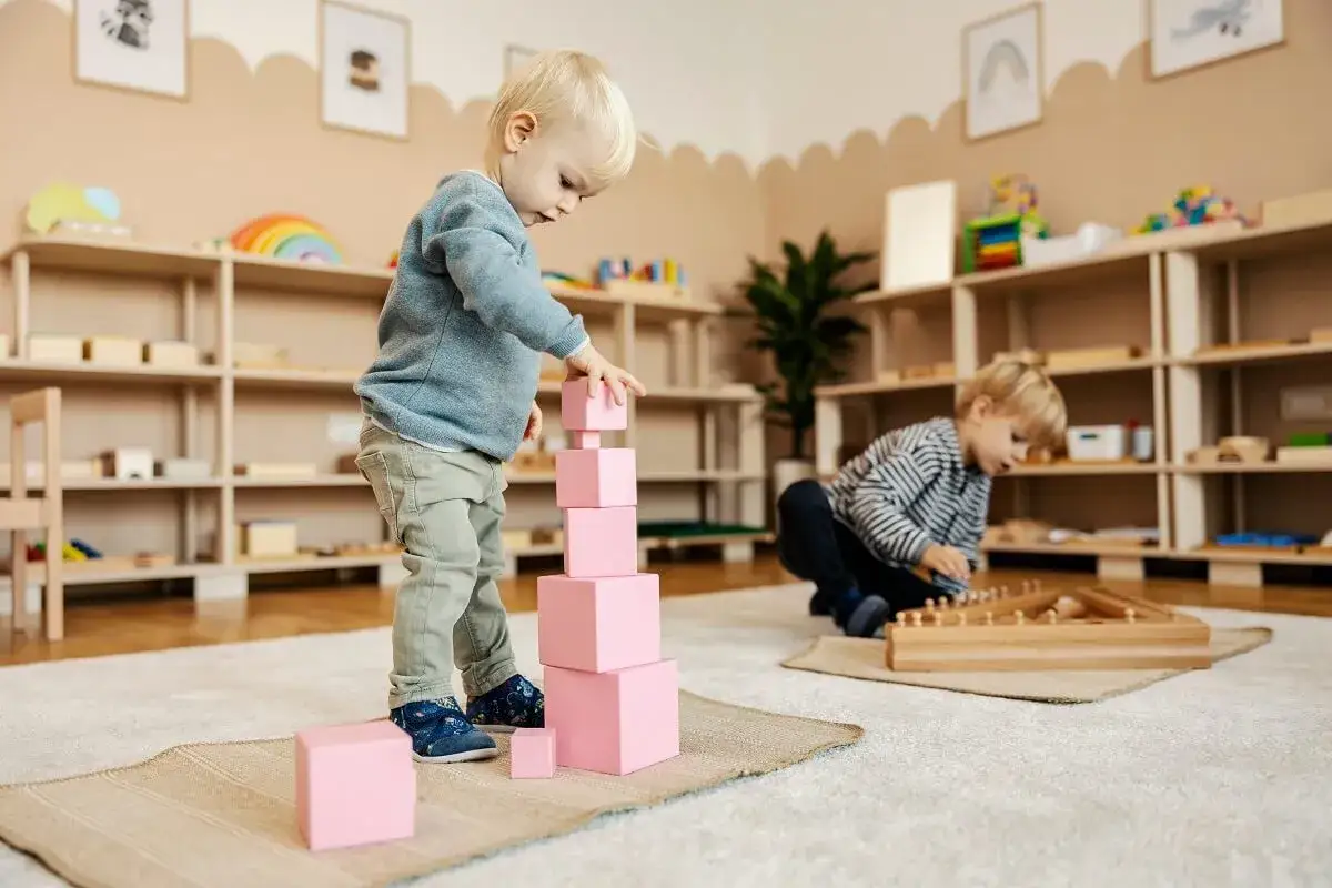 Dzieci bawią się klockami, rozwijając zdolności manualne i logiczne. To przykład edukacji metodą Montessori, gdzie nauka odbywa się przez zabawę.