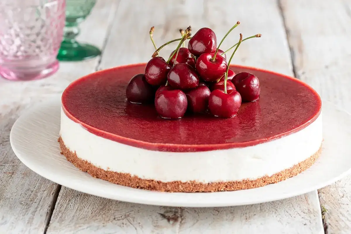 Delizioso cheesecake alle ciliegie, con uno strato cremoso bianco e una copertura rossa brillante, guarnito con ciliegie fresche.
