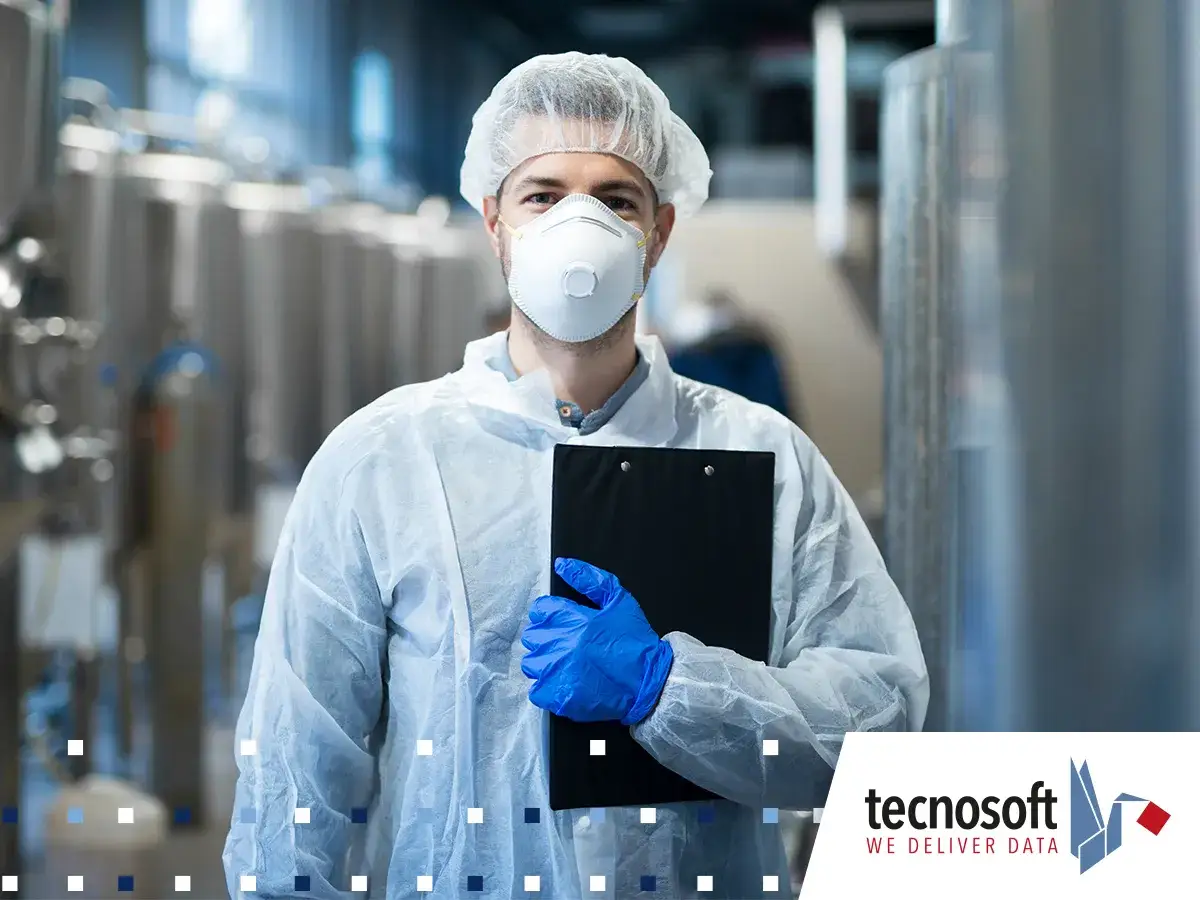Un tecnologo alimentare in tuta, mascherina e guanti tiene una cartella in un impianto di produzione.