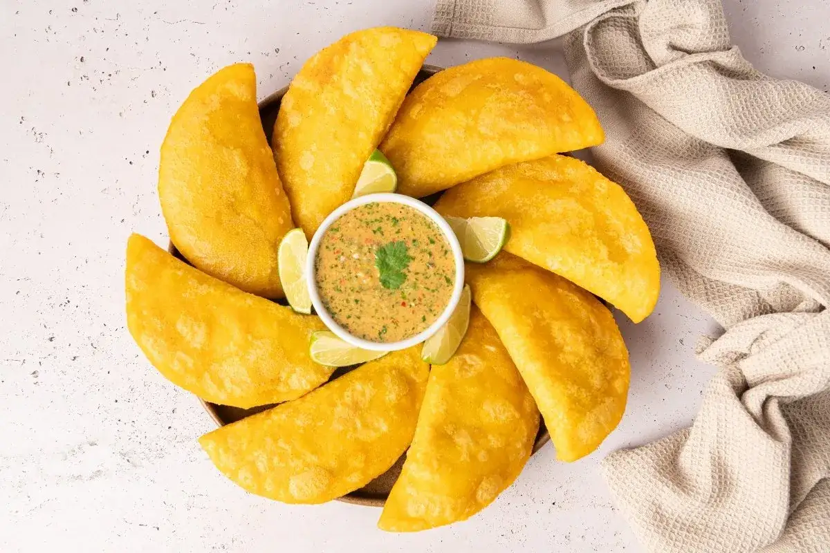Un plato circular con empanadas colombianas doradas y crujientes, acompañadas de una salsa picante y gajos de limón.