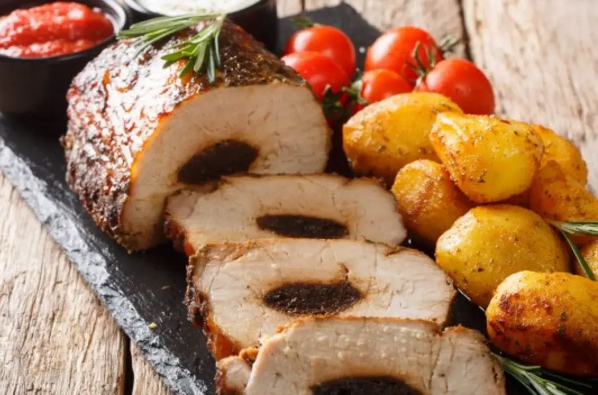 Pyszny schab na obiad, faszerowany śliwkami, podany z pieczonymi ziemniaczkami i pomidorkami.