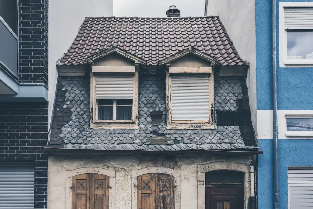 Stary dom z łupkowym dachem i okiennicami. Jak zrobić odbiór domu po 20 latach? Warto sprawdzić stan dachu i elewacji.