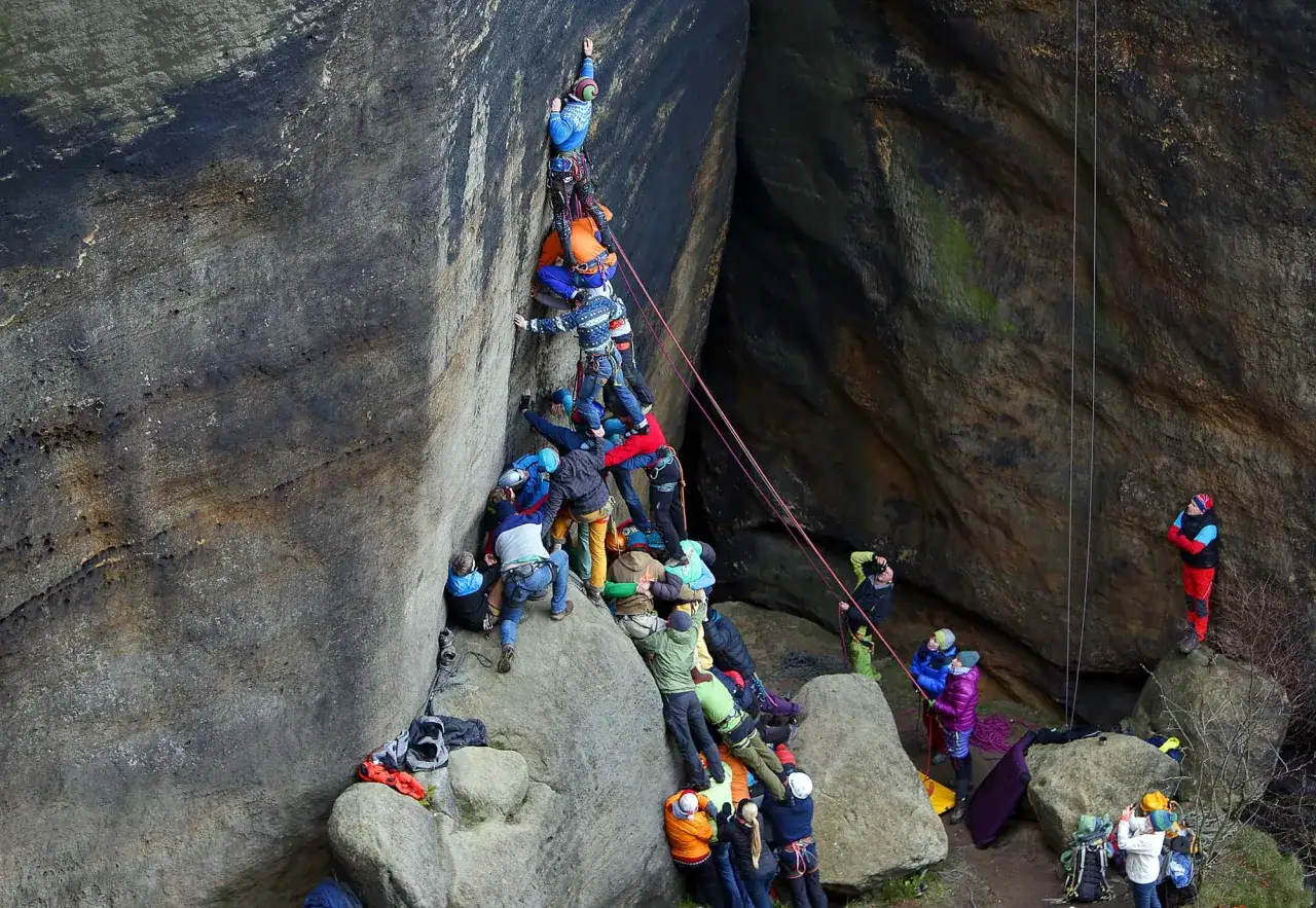 Eine Gruppe von Kletterern in Tschechien bildet eine menschliche Leiter, um einen Felsen zu erklimmen.