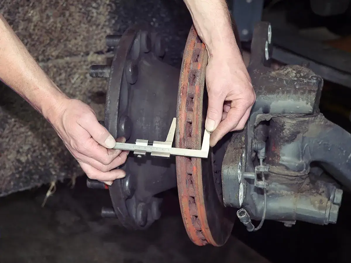 Mechanik mierzy suwmiarką zużytą tarczę hamulcową, sprawdzając jej minimalną grubość.