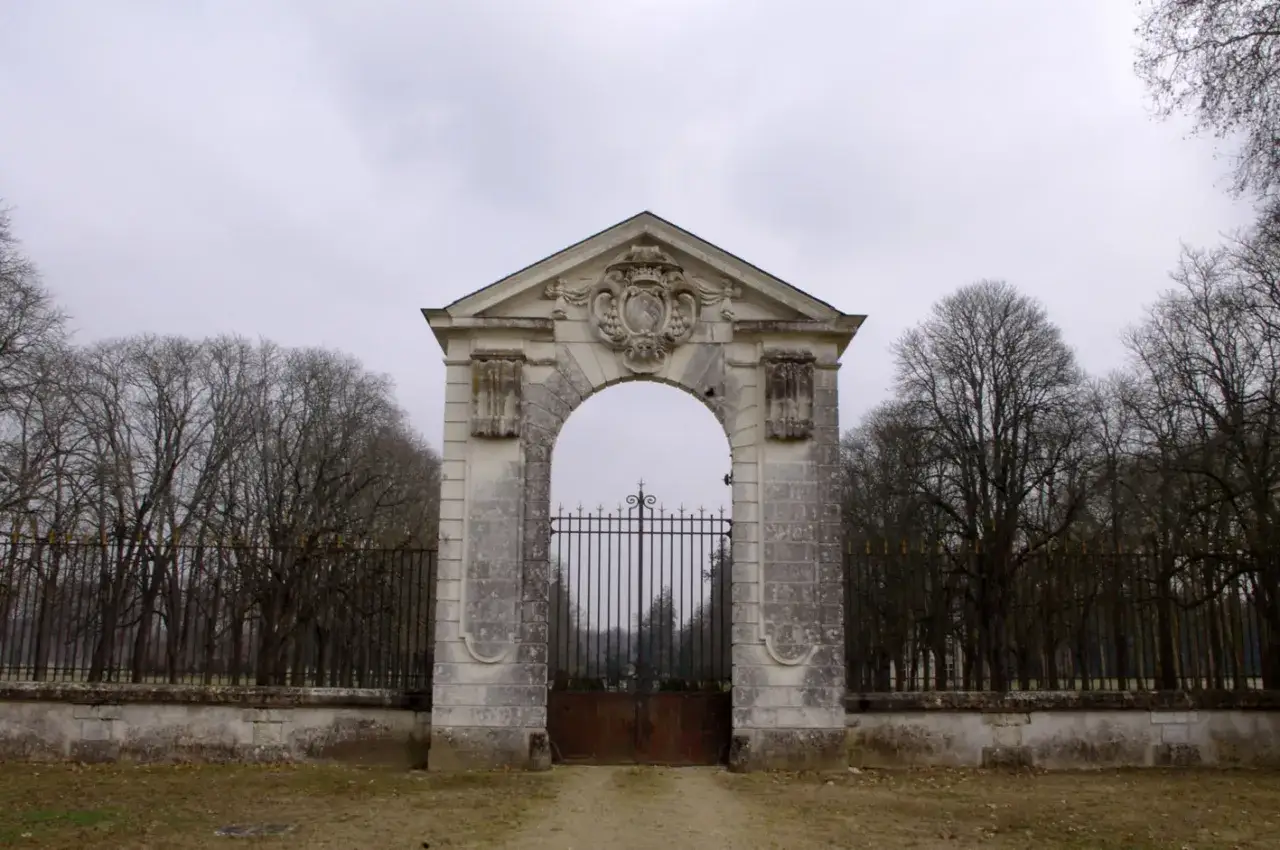 Portail monumental menant au **château de Richelieu**, orné d'un blason. Arbres dénudés et ciel gris.