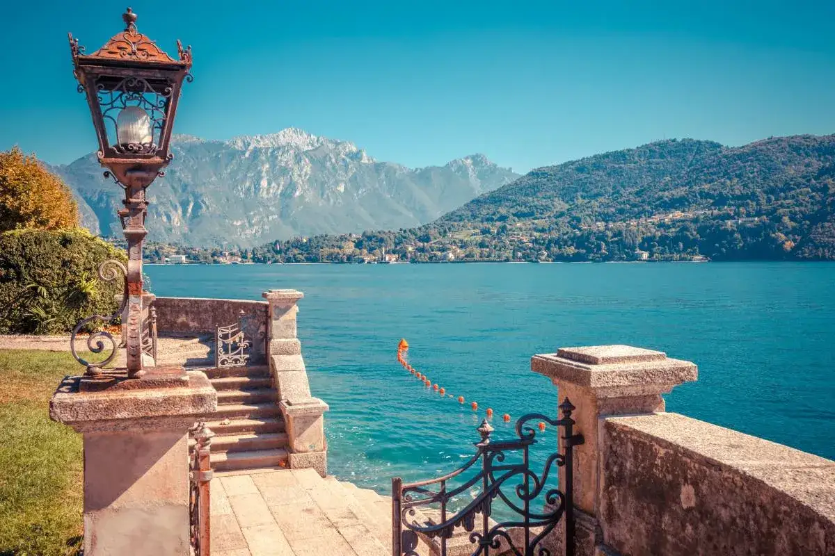 Un perfetto weekend sul Lago di Como: scalinata in pietra, lampione antico e vista mozzafiato sulle montagne e sul lago azzurro.