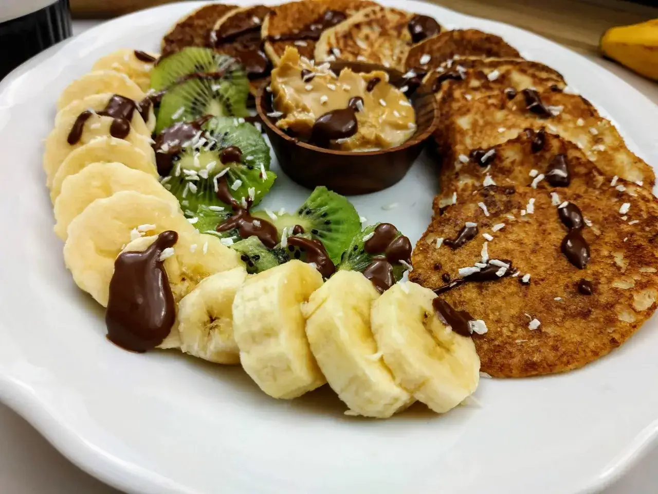 Idealne śniadanie na słodko: placuszki z bananami, kiwi, masłem orzechowym i polewą czekoladową.